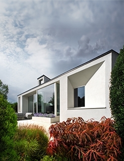 Modern residential rebuild project in South Dublin with flat roof and large floor-to-ceiling windows, set amongst a garden with red-leafed plants and a stormy sky overhead